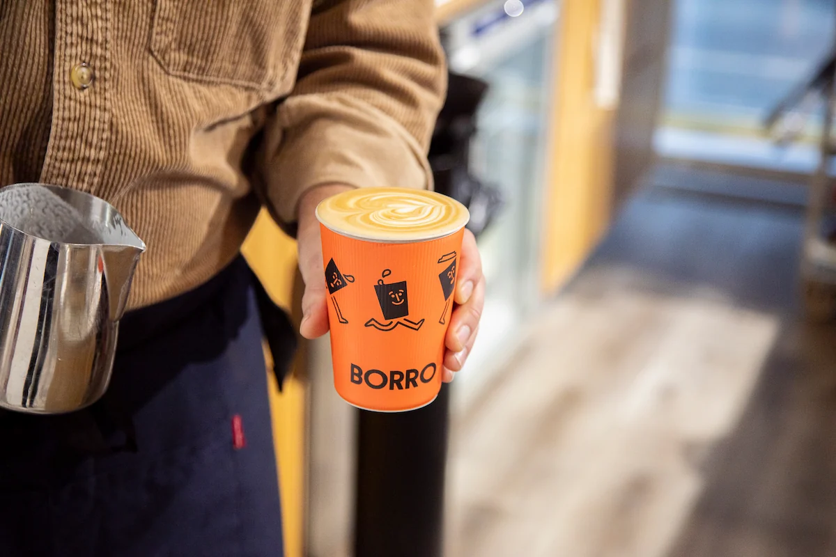 Photo of a barista holding a milk jug and a nicely poured latte with artwork on top